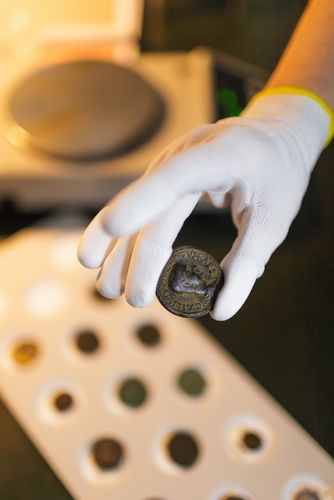 Nahaufnahme auf eine antike Münze, die mit Handschuhe gehalten wird, Foto: Christian Hüller