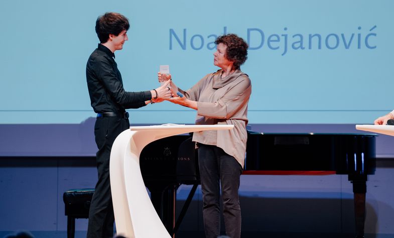 Noah Dejanović bekommt von Beate Schücking den Preis auf der Bühne überreicht.