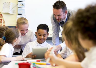 Ein männlicher Lehrer beaufsichtigt eine Gruppe von Schülern, die an digitalen Tablets arbeiten.