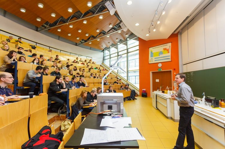 Querschnitt auf die gefüllten Hörsaalreihen links und rechts auf Prof. Harald Krautscheid mit Tafel und Experimentiertische, Foto: Christian Hüller