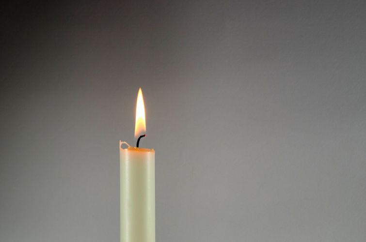 Brennende Kerze vor grauem Hintergrund
