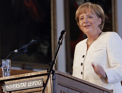 Foto: Dr. Angela Merkel steht am Rednerpult, in einem weißem Jacket gekleidet mit freudigem Gesichtsausdruck
