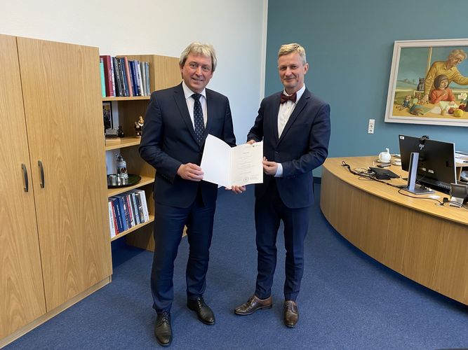 Wissenschaftsstaatssekretär Dr. Andreas Handschuh überreicht Dr. Jörg Wadzack eine Urkunde in einem Büro