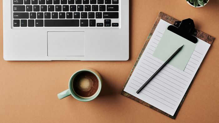 Eine Tasse Kaffee steht neben einem Laptop und einem Block