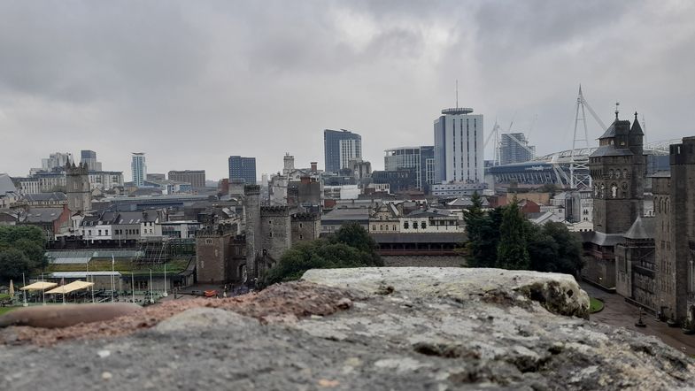 Blick auf die Stadt Cardiff bei bedecktem Himmel. Es sind Hochhäuser, Wohnhäuser und rechts ein Fußballstadion zu sehen.
