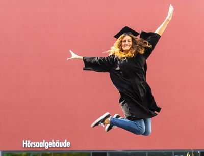 Eine Studentin im schwarzen Talar springt in die Luft vor Freude, Foto: Christian Hüller