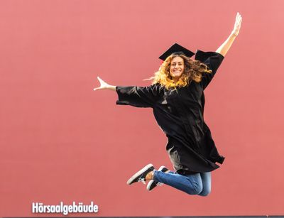 Eine Studentin im schwarzen Talar springt in die Luft vor Freude, Foto: Christian Hüller