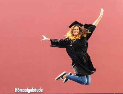 Eine Studentin im schwarzen Talar springt in die Luft vor Freude, Foto: Christian Hüller