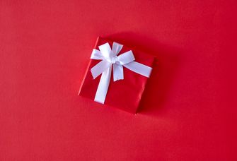 Auf einem roten Hintergrund liegt ein ebenfalls rotes Paket, welches mit einer weißen Schleife wie ein Geschenkeingepackt ist.