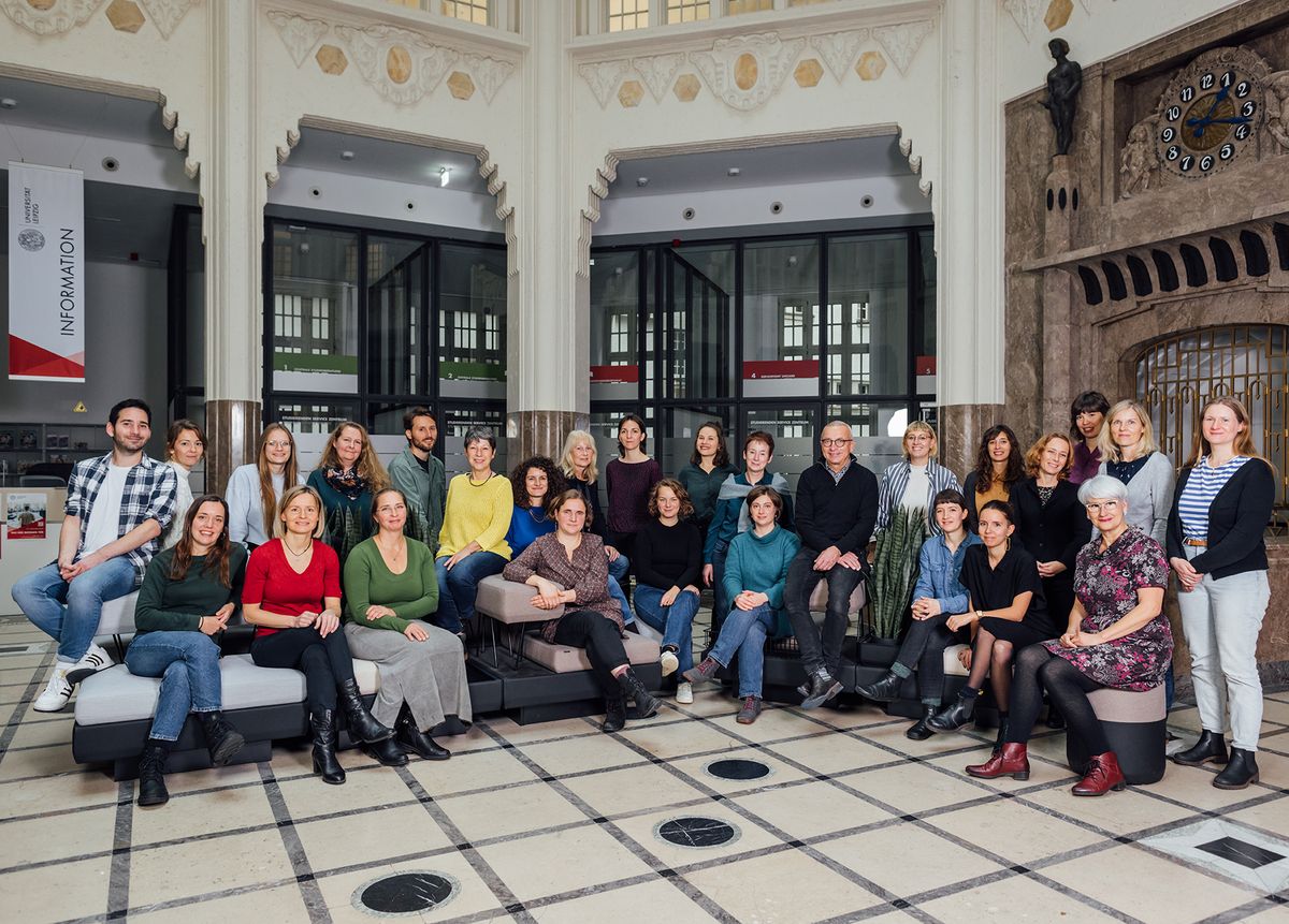 enlarge the image: Colour photo: Staff of the International Office sitting or standing together in the foyer of the SSZ at the University of Leipzig.