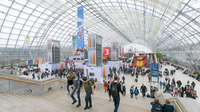 Im lichtdurchflutetem Foyer der Leipziger Messe laufen mehrere Besucher der Buchmesse die Treppe hinauf.