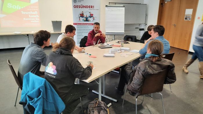 Eine Personengruppe sitzt um einen Tisch und diskutiert