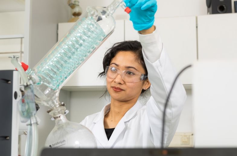 Eine Wissenschaftlerin steht im Labor und hält in ihrer Hand einen Rotationsverdampfer
