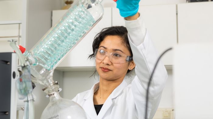 Eine Wissenschaftlerin steht im Labor und hält in ihrer Hand einen Rotationsverdampfer