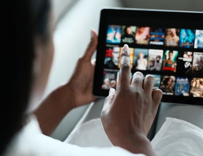 Auf dem Foto ist die Hand einer Frau zu sehen, die ein Tablet hält, auf dem Netflix geöffnet ist.