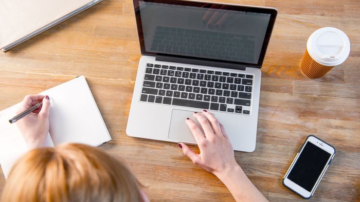 Junge Frau von oben gesehen sitzt am Laptop und macht sich Notizen.