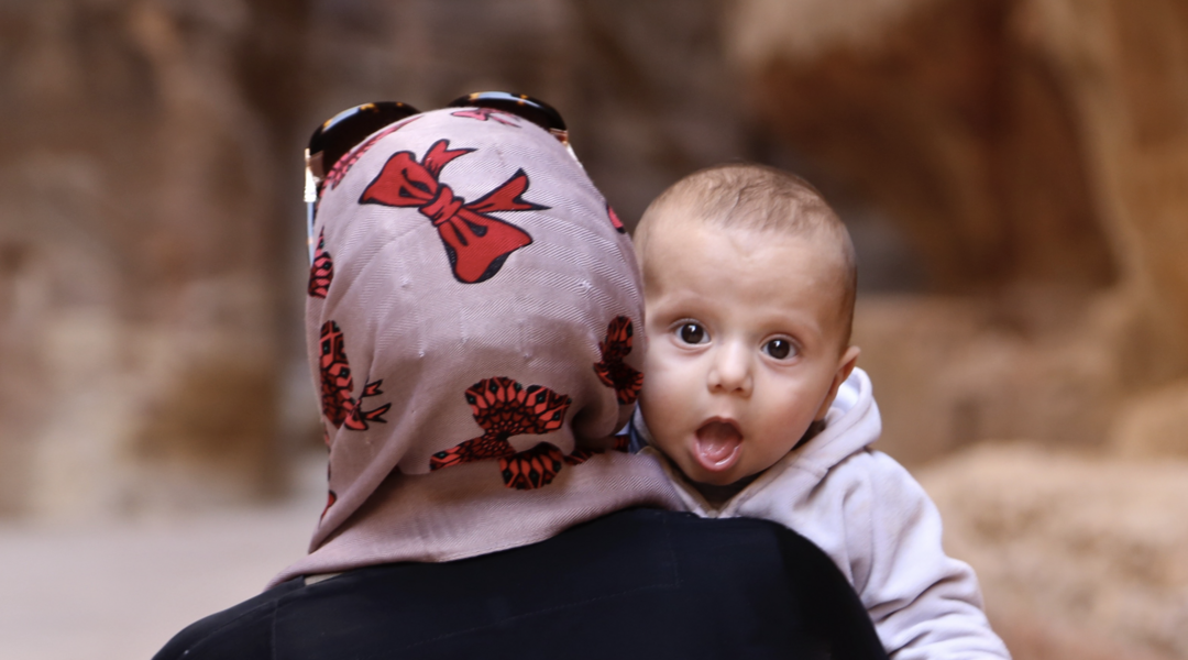 Rückenansicht einer Frau mit Kopftuch und Kind auf dem Arm, das einen erstaunt und neugierig anschaut, Foto: Frank Lütze