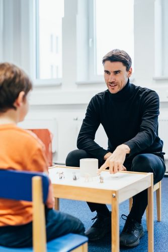 Ein Mann sitzt an einem Kindertisch und redet mit einem Kind