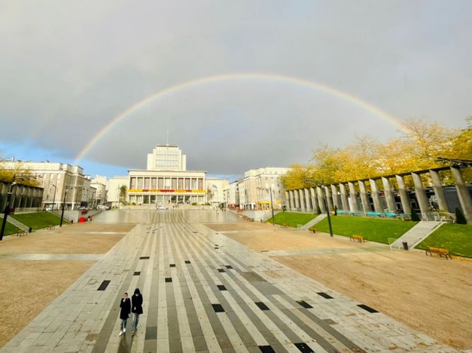 Das sowjetisch anmutende Rathaus der Stadt Brest ist im Hintergrund zu sehen. Darüber ist ein Regenbogen. Im Vordergrund ist ein großer, leerer Platz.
