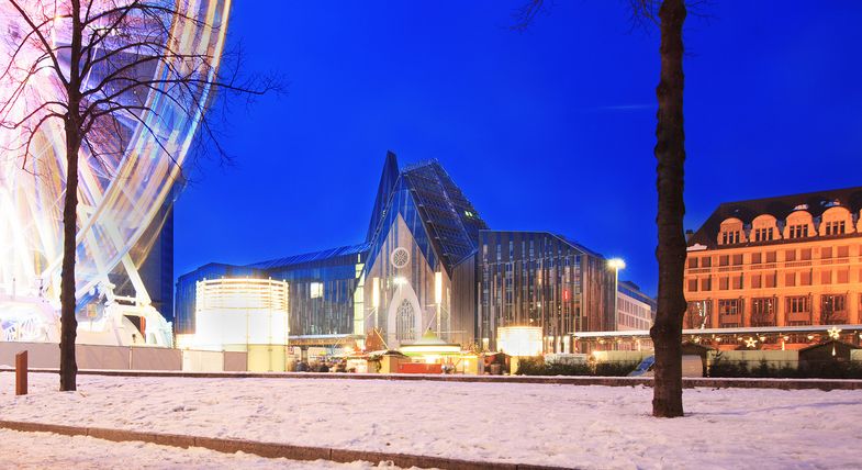 Foto: Seitliche Ansicht auf das Hauptgebäude der Universität am Campus Augustusplatz in weihnachtlicher Atmosphäre und Lichterbogen vom Riesenrad.