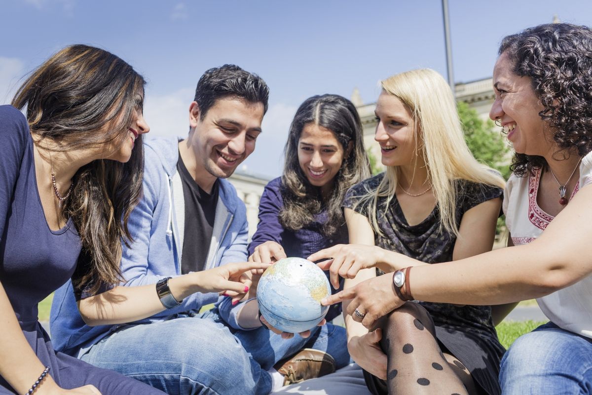 zur Vergrößerungsansicht des Bildes: Foto: Eine Gruppe internationaler Studierender betrachtet eine Weltkugel und zeigen sich gegenseitig ihre Heimatländer