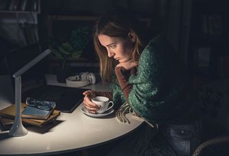 Eine Frau sitzt lustlos und mit einer Tasse in der Hand vor dem Laptop.