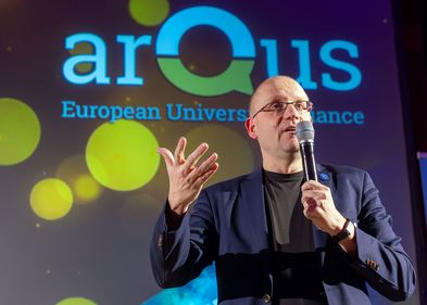 Professor Utz Dornberger spricht in ein Mikrofon und steht dabei vor einem Banner mit der Aufschrift Arqus.