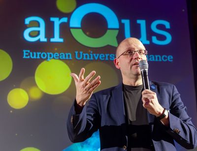 Professor Utz Dornberger spricht in ein Mikrofon und steht dabei vor einem Banner mit der Aufschrift Arqus.