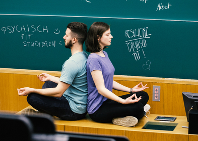 Zwei Studierende sitzen im Vorlesungssaal und meditieren