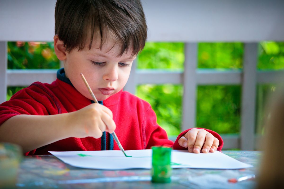 Zu sehen ist ein kleiner Junge, der sich auf das Bild, das er gerade malt, konzentriert.