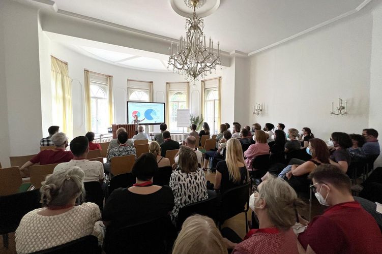 in einem großen Raum sitzen viele Zuhörer:innen und hören einen Vortrag.
