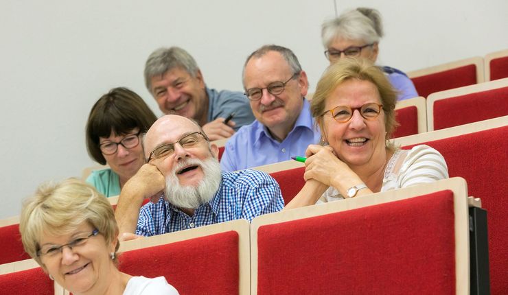 Lächelnde Teilnehmerinnen und Teilnehmer des Seniorenkollegs im Audimax