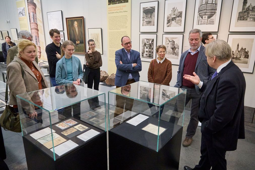 zur Vergrößerungsansicht des Bildes: Förderer und Stipendiaten stehen um eine Glasvitrine in der Galerie im Neuen Augusteum und hören dem Kustos, der vor den Gästen steht, zu