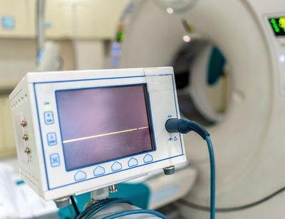 Detailaufnahme eines Computer-Tomographie-Geräts. Im Vordergrund ist ein Anzeigegerät mit Verkabelung zu sehen. 
