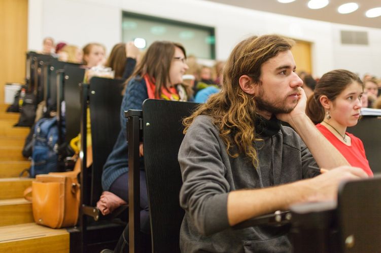 Blick vom Durchgang unten auf die hintereinanderliegenden Sitzreihen. Studierende schauen Richtung Pult, Foto: Christian Hüller 