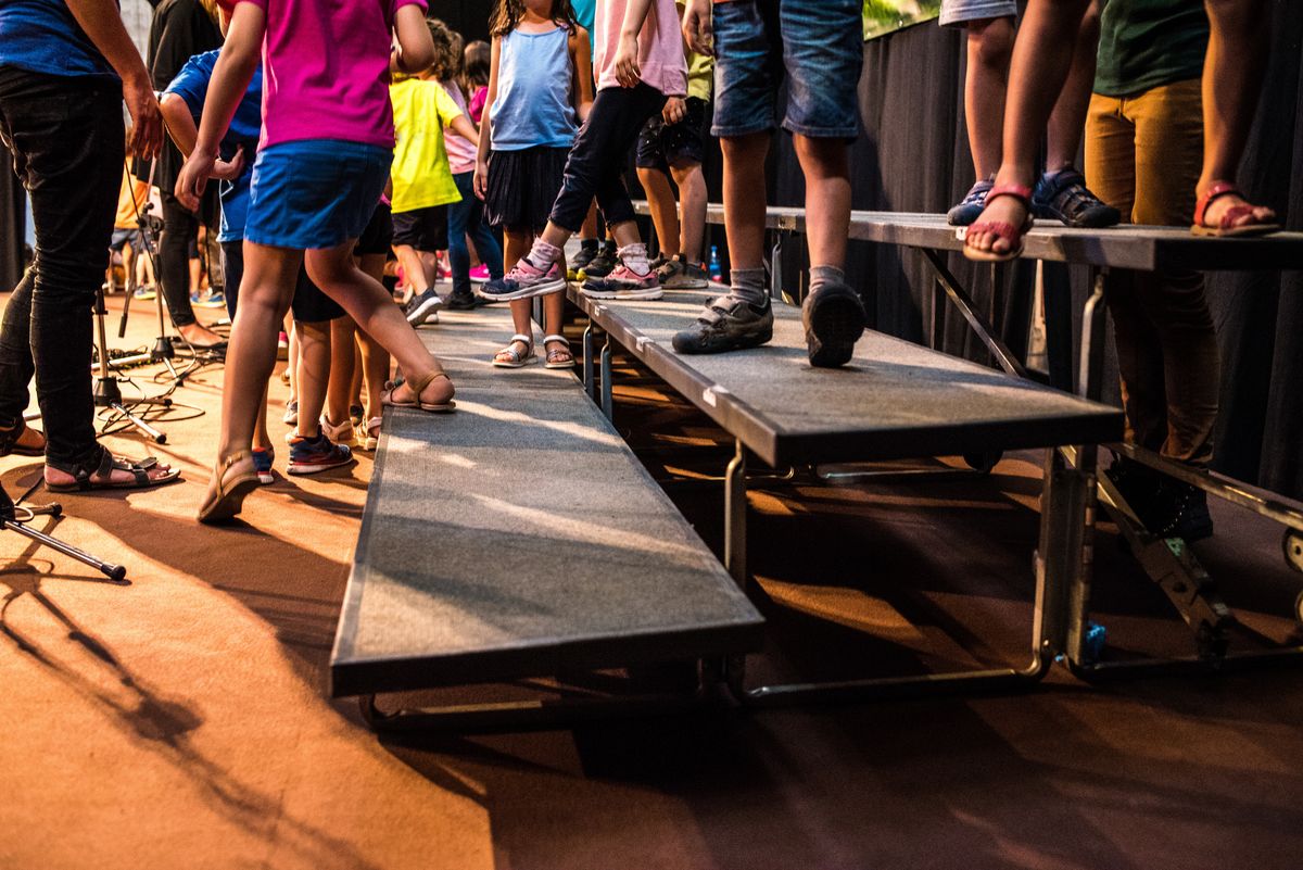 zur Vergrößerungsansicht des Bildes: Auf dem Bild sind die Beine von Kindern, die gemeinsam auf einer Bühne stehen, zu sehen.