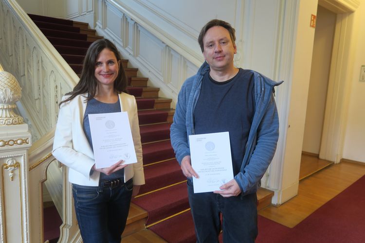 Alina Fichter und Lorenz Matzat zeigen ihre Berufungsurkunden im Foyer des Rektoratsgebäudes.