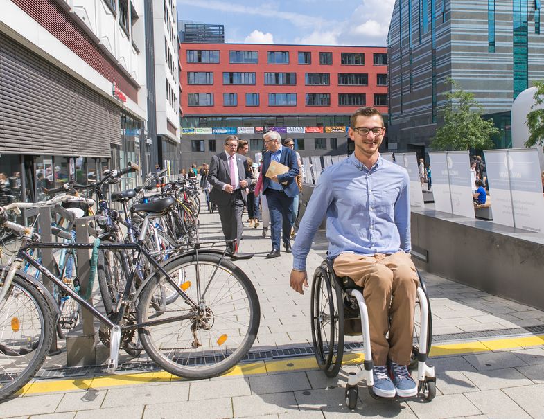 Auf dem Bild ist ein junger Rollstuhlfahrer im Innenhof des Campus Augustusplatz zu sehen.