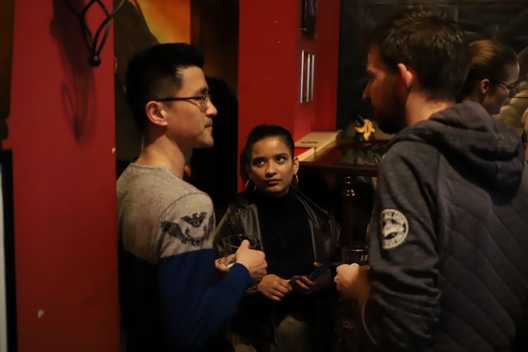 two men and one woman standing in circle in a cafe 