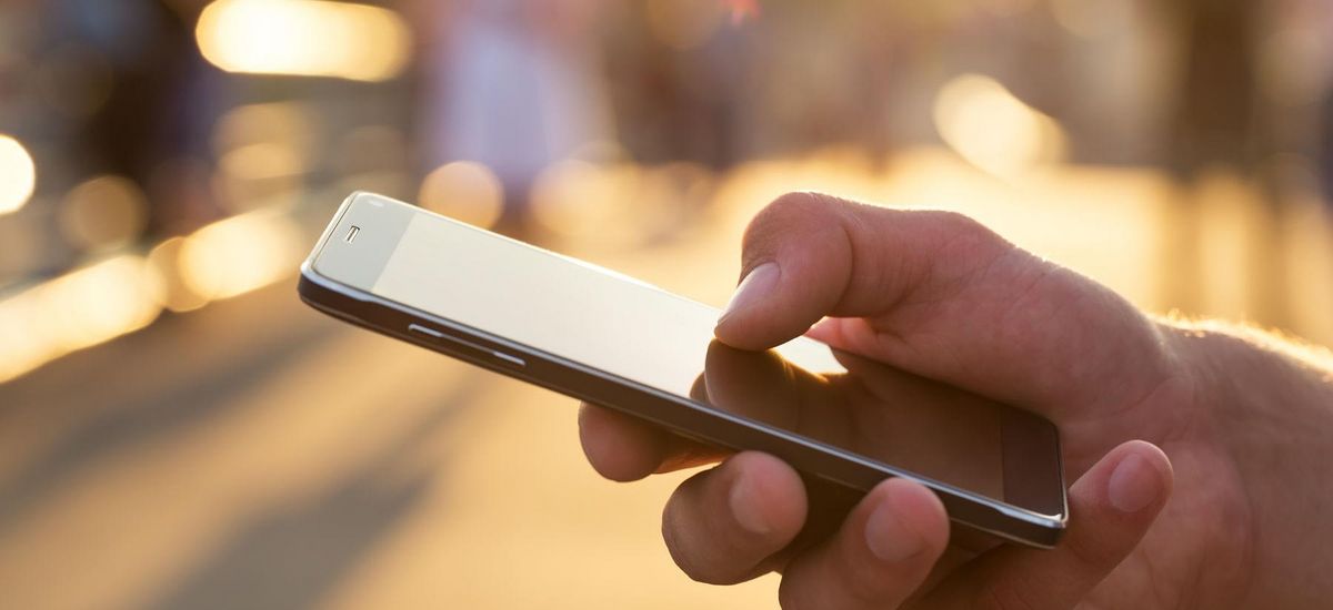 Nahaufnahme einer Hand, die ein Smartphone hält. Im Hintergrund helles Sonnenlicht.