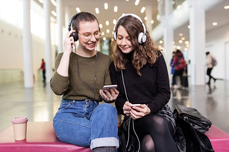 2 Studentinnen hören gemeinsam etwas mit Kopfhörern