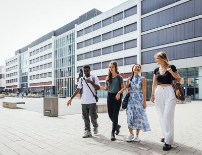 Colour photo: Four people walking across the inner courtyard of the university and talking
