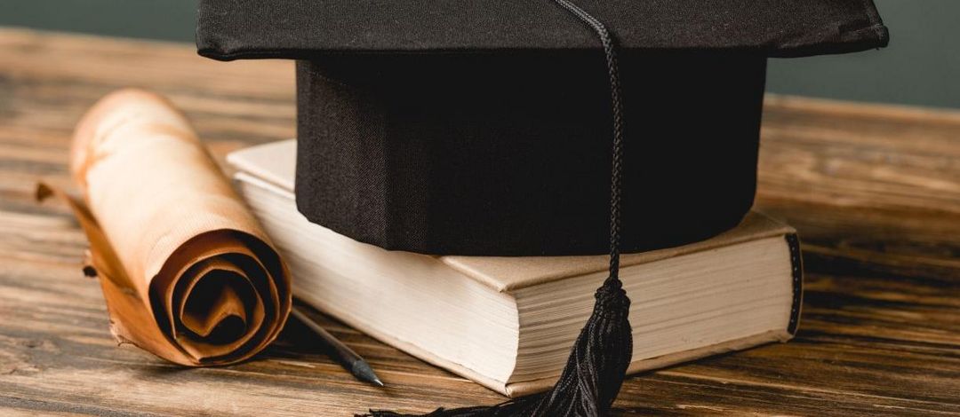 Ein Buch mit Doktorhut und Schriftrolle liegen auf einem Tisch