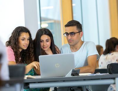 Internationale Studierende schauen zusammen in einen Laptop