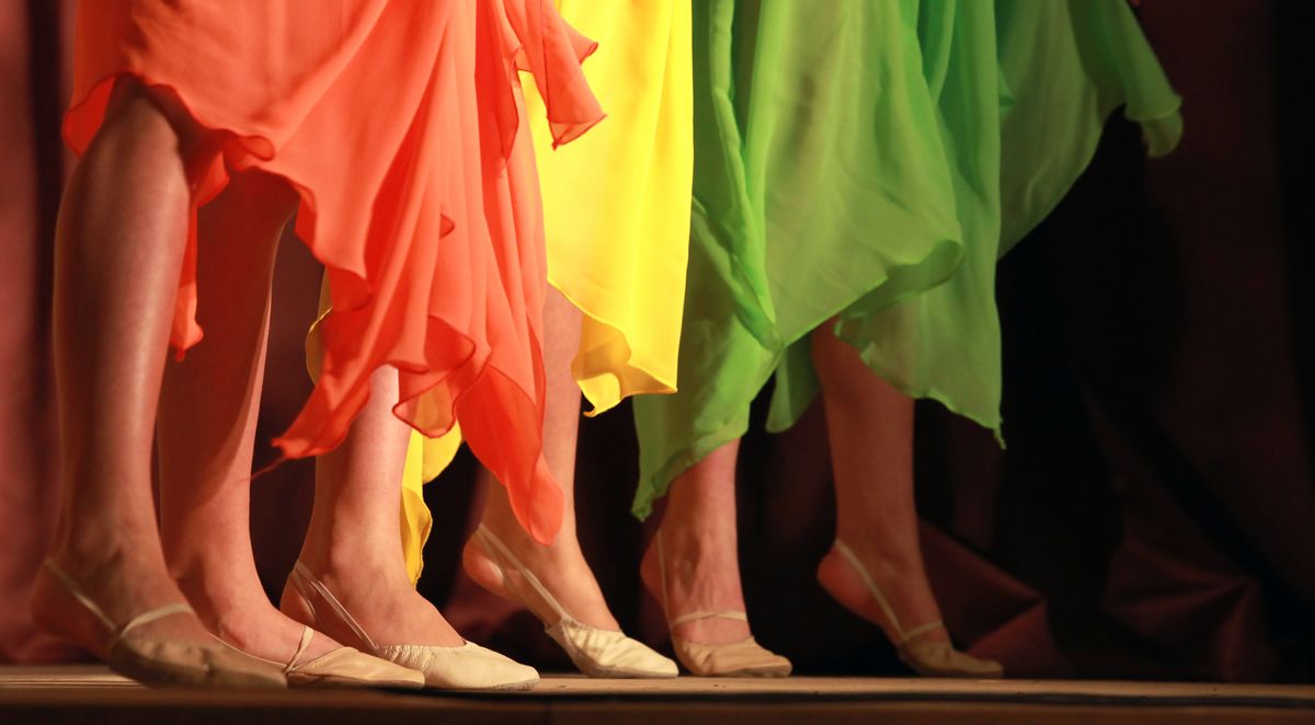 Drei Personen tanzen in bunten Tüchern auf einer Bühne. Man sieht nur ihre Beine