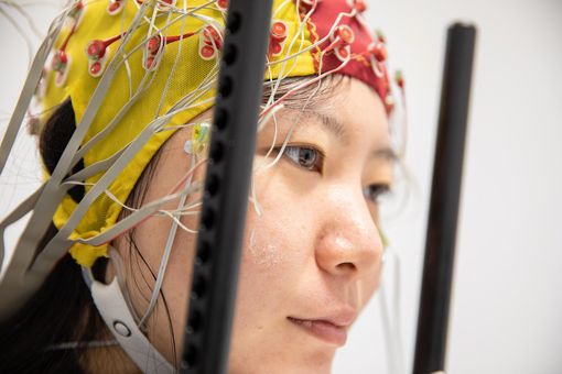 Eine Testperson mit angebrachter EEG-Haube, welche die simultane Spannungsmessung an 64 Stellen der Kopfoberfläche ermöglicht..
