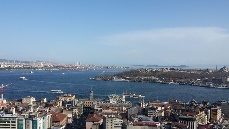 Durch die Bildmitte schlängelt sich die breite Meerenge "Bosporus". An drei Stellen ist die Stadt Istanbul zu sehen, bestehend aus modernen Hochhäusern, Moscheen und Wohnhäusern.