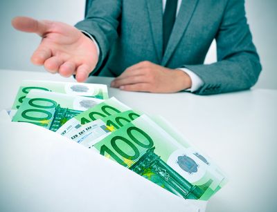 Briefumschlag mit 100-Euro-Scheinen und Person im Anzug im Hintergrund, die die rechte Hand gebend ausstreckt