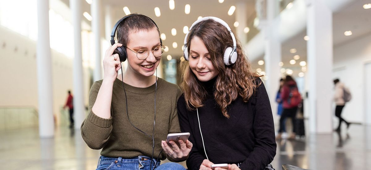 Zwei Studentinnen mit großen Kopfhörern hören in Neuen Augusteum der Uni Leipzig den neuen Podcast "Auf einen Kaffee mit...", Foto: Christian Hüller