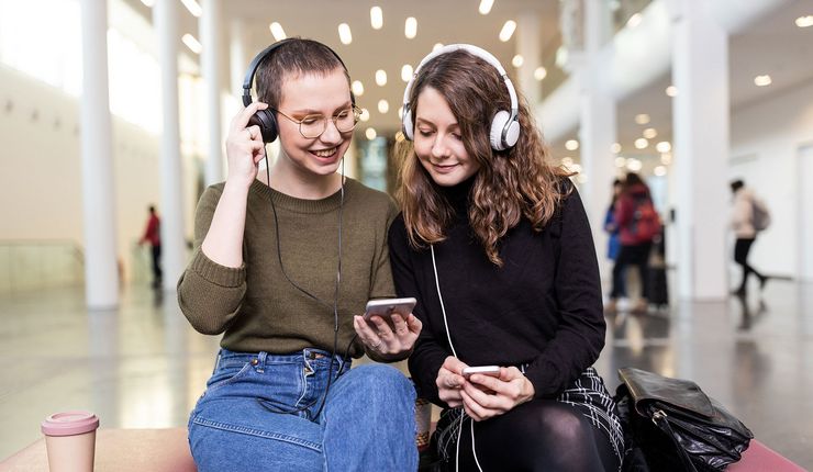 Zwei Studentinnen mit großen Kopfhörern hören in Neuen Augusteum der Uni Leipzig den neuen Podcast "Auf einen Kaffee mit...", Foto: Christian Hüller